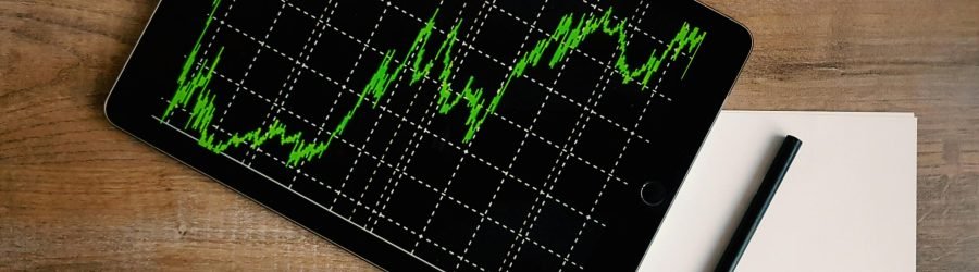 Flatlay of an iPad displaying stock market graph on a wooden desk with a pencil and paper.